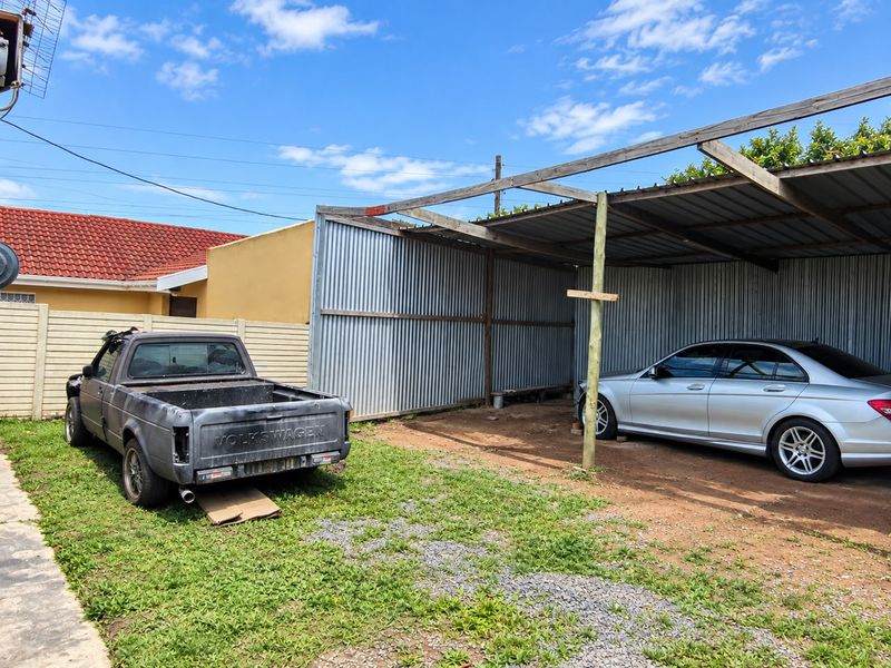 An open-sided carport structure featuring corrugated metal wall cladding and a timber frame, situated in a residential backyard area.