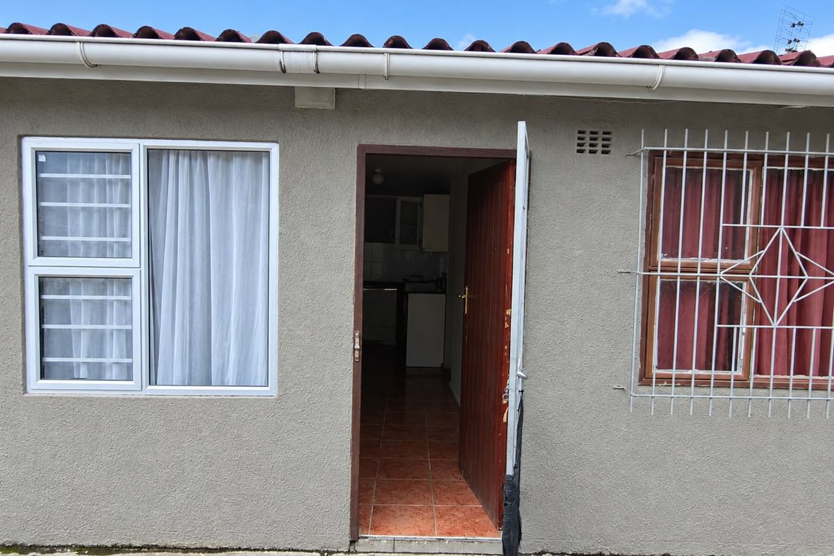 Exterior view of a rear entrance featuring plastered walls, security bars on windows, and a tiled roof with guttering.