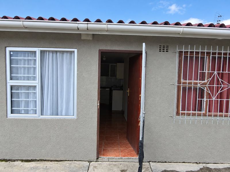 Exterior view of a rear entrance featuring plastered walls, security bars on windows, and a tiled roof with guttering.