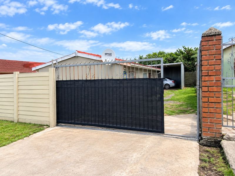 Front view of the property featuring a sliding gate, concrete driveway, and a carport, enclosed by a combination of brick and precast concrete walls.