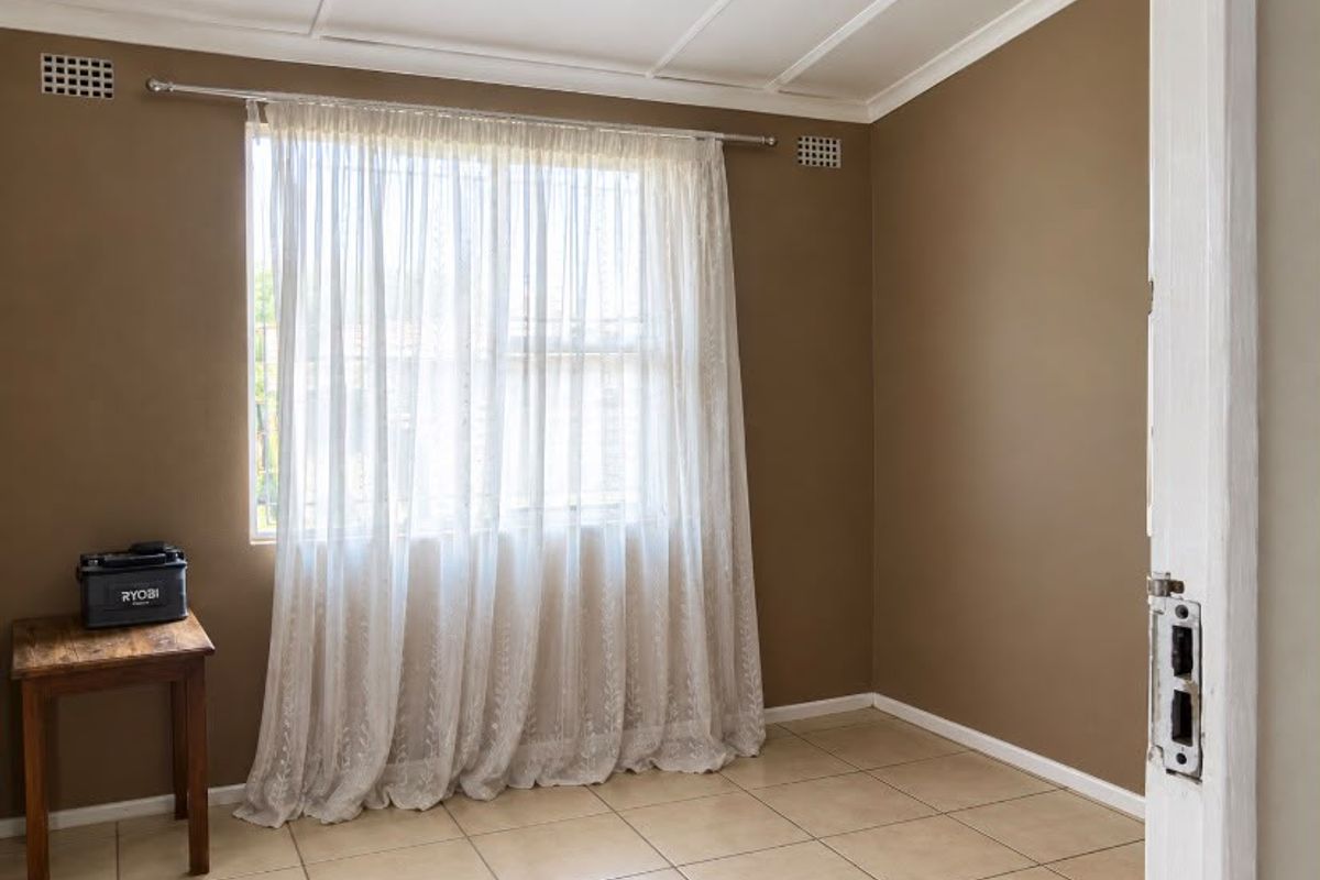 A vacant bedroom featuring neutral wall tones, tiled flooring, and a window with sheer curtains.