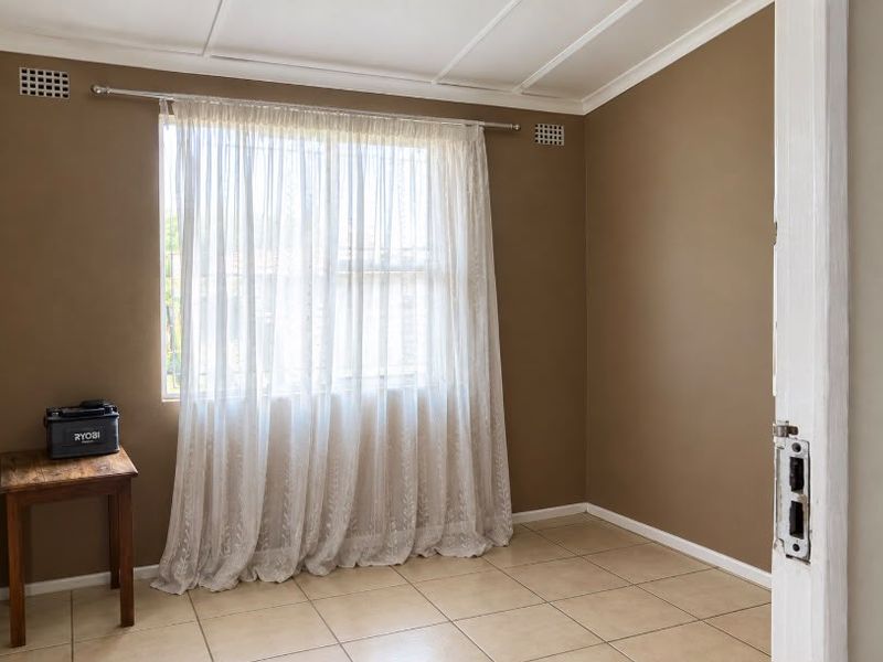 A vacant bedroom featuring neutral wall tones, tiled flooring, and a window with sheer curtains.