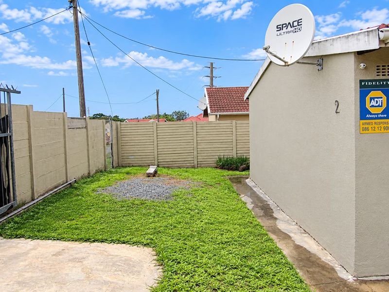 A rear exterior view of the property featuring a small lawn area, concrete boundary walls, and a mounted satellite dish.