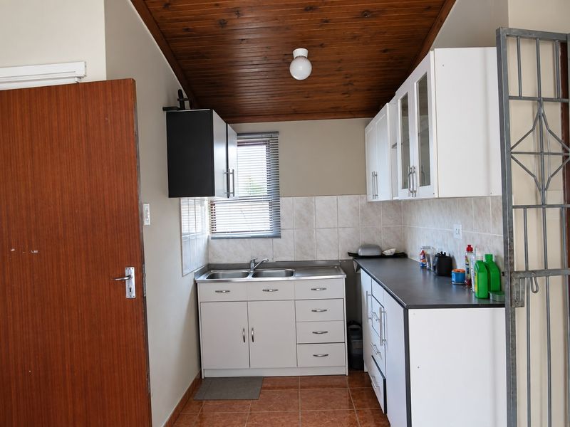A functional scullery area featuring built-in cabinetry, a double stainless steel sink, tiled backsplash, and a distinctive timber ceiling.