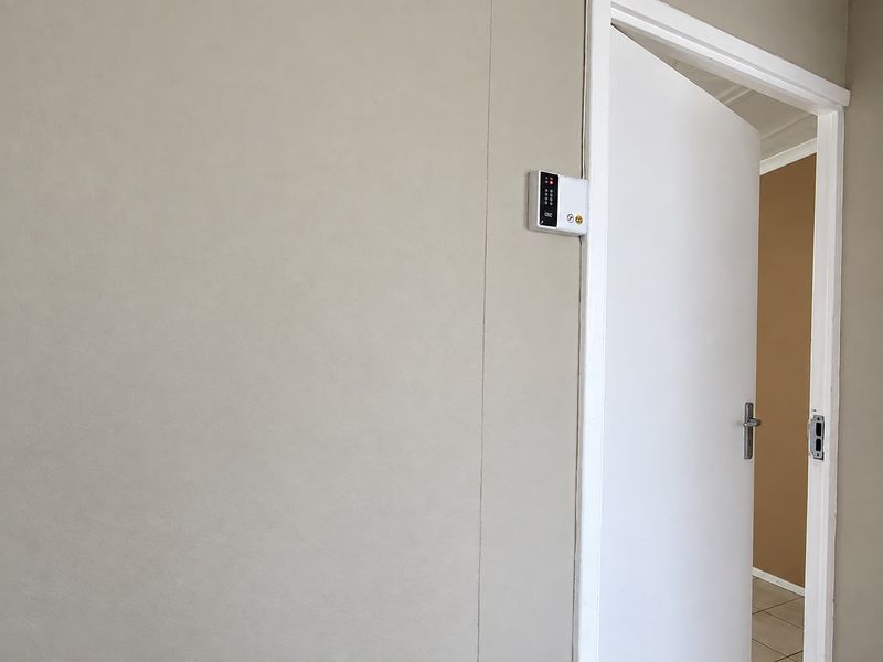 A neutral-toned hallway featuring a wall-mounted security alarm keypad and a white interior door leading to an adjacent room.