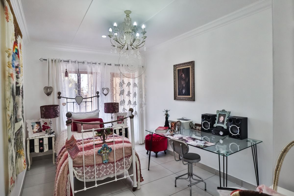 A well-maintained bedroom featuring neutral tiled flooring, decorative crown molding, and a central chandelier, providing a bright and functional living space.