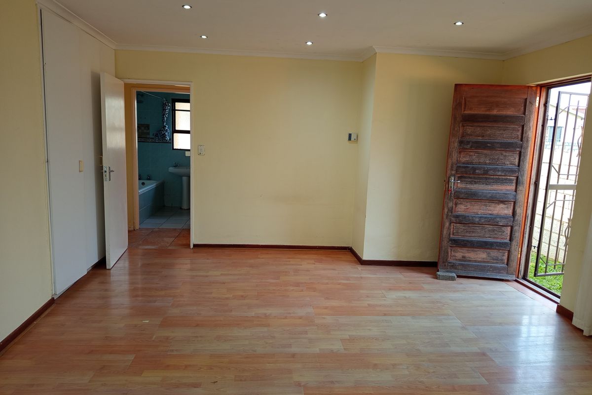 An empty bedroom featuring laminate flooring, recessed downlights, and built-in cupboards, with direct access to an en-suite bathroom and an exterior entrance.