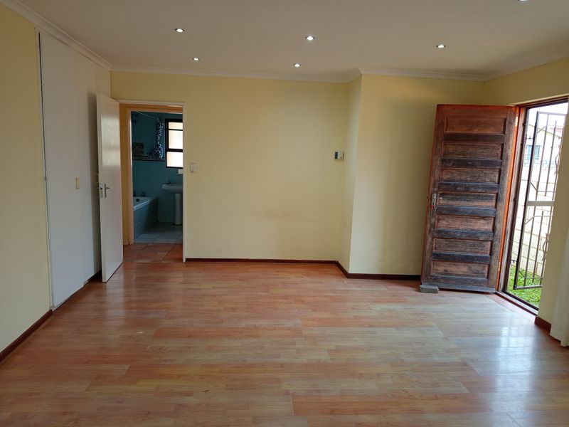 An empty bedroom featuring laminate flooring, recessed downlights, and built-in cupboards, with direct access to an en-suite bathroom and an exterior entrance.