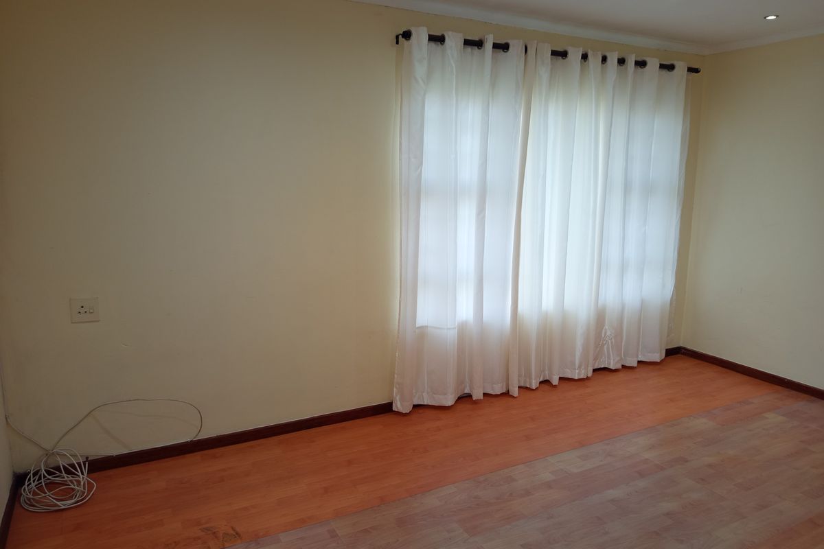 An empty living room featuring laminate flooring, recessed downlighting, and neutral walls, providing a blank canvas for interior design.
