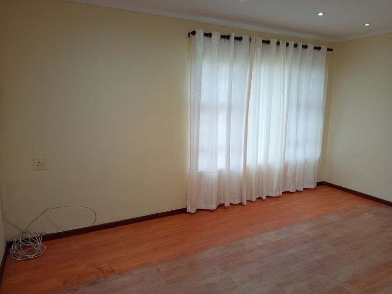 An empty living room featuring laminate flooring, recessed downlighting, and neutral walls, providing a blank canvas for interior design.