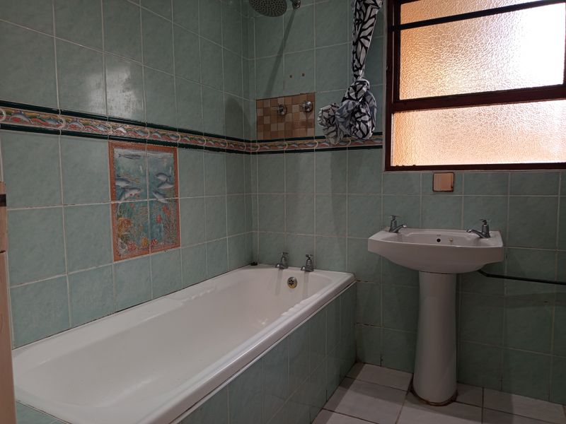 A dated bathroom featuring a pedestal basin, built-in bathtub, and wall-mounted shower head, finished with decorative tiled walls and flooring.