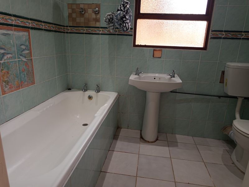 A dated bathroom featuring a pedestal basin, bathtub, and toilet with light green wall tiles and white floor tiles.