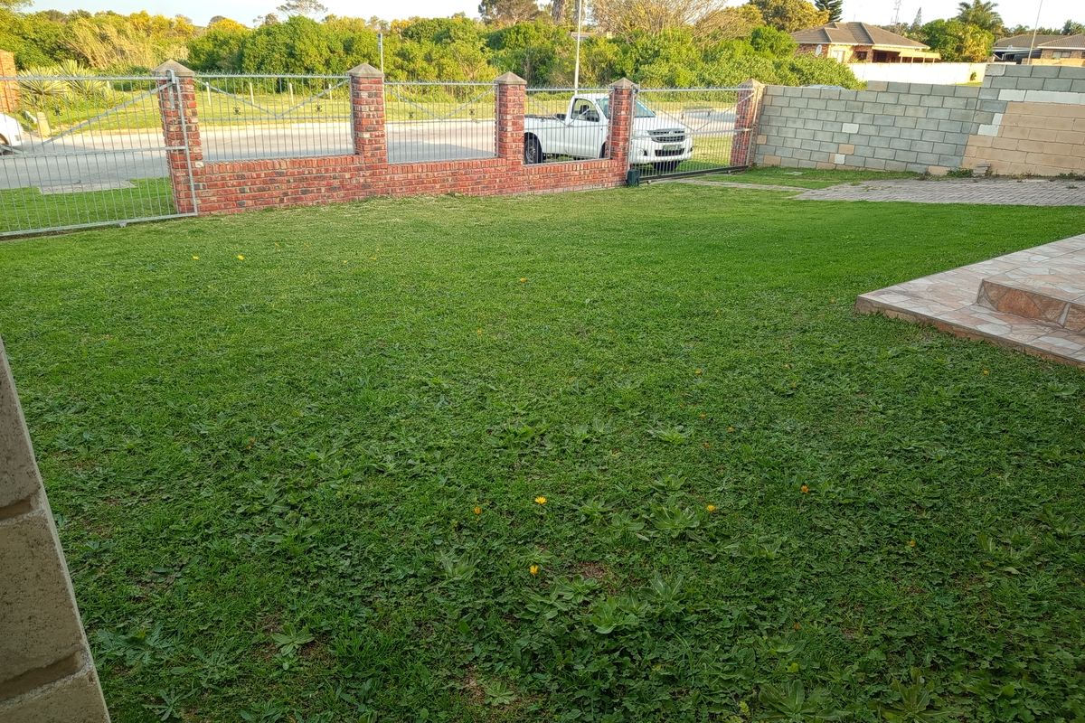 A rear garden area featuring a lawn, paved patio section, and a brick and metal boundary fence.