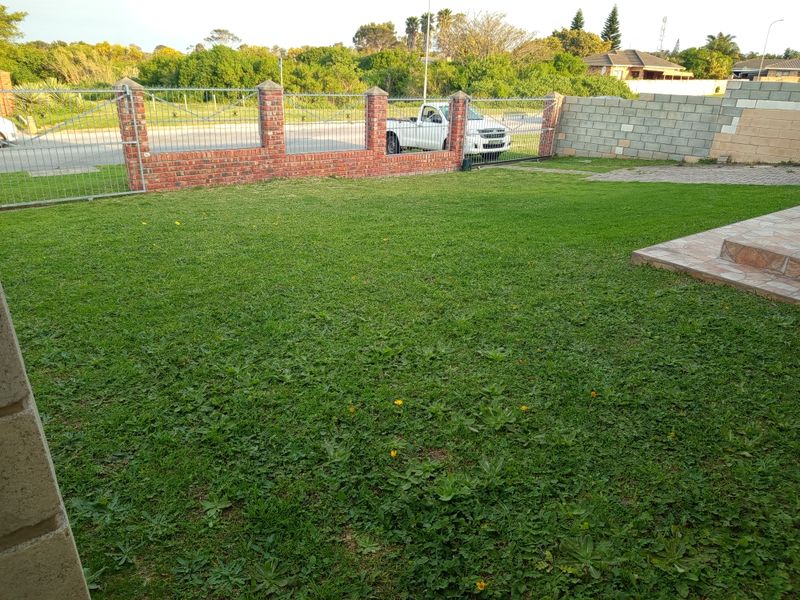 A rear garden area featuring a lawn, paved patio section, and a brick and metal boundary fence.