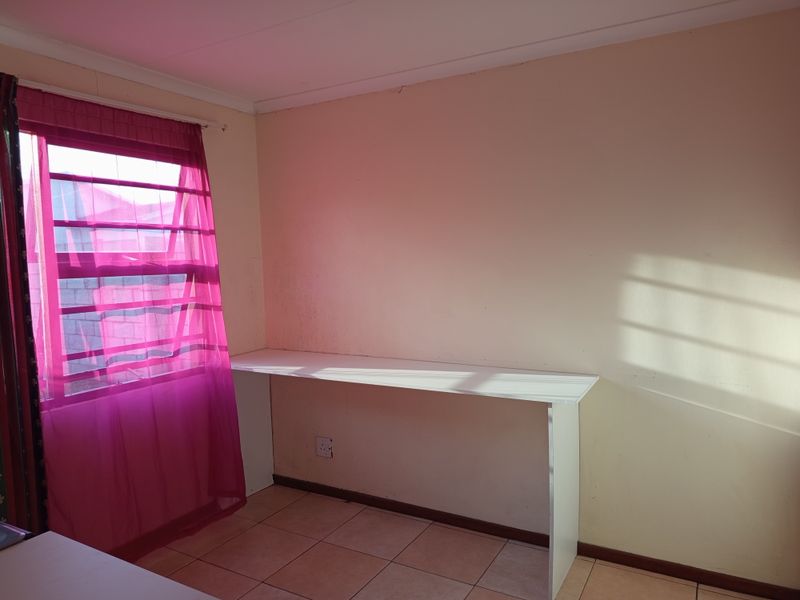 A simple bedroom featuring tiled flooring and a built-in desk, offering a functional space ready for personalization.