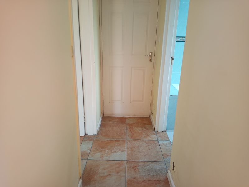 A narrow hallway featuring tiled flooring and access to adjacent rooms, showing signs of wear on the skirting boards and walls.