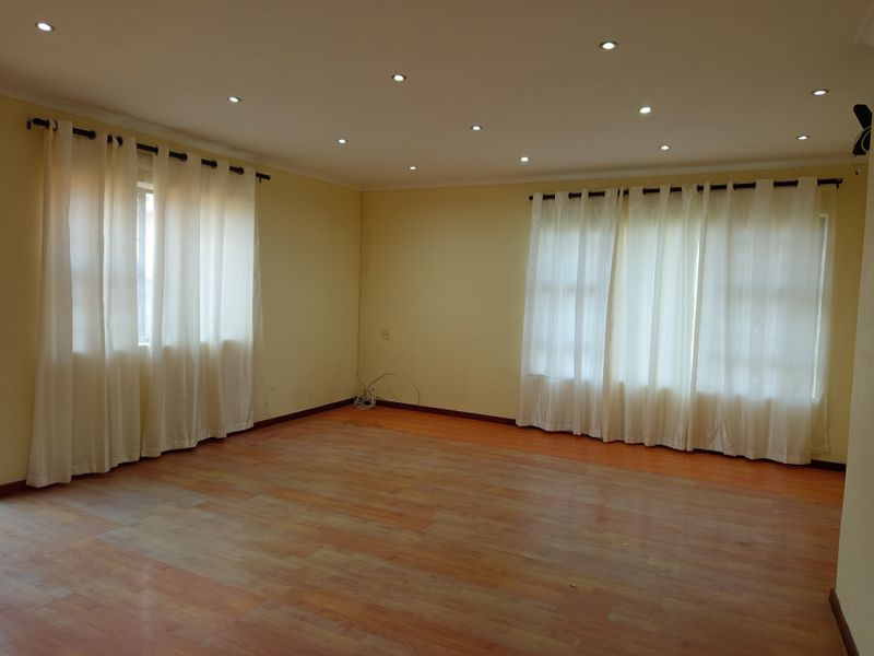 A spacious, empty living room featuring laminate flooring, recessed downlights, and large windows with installed curtain rods.