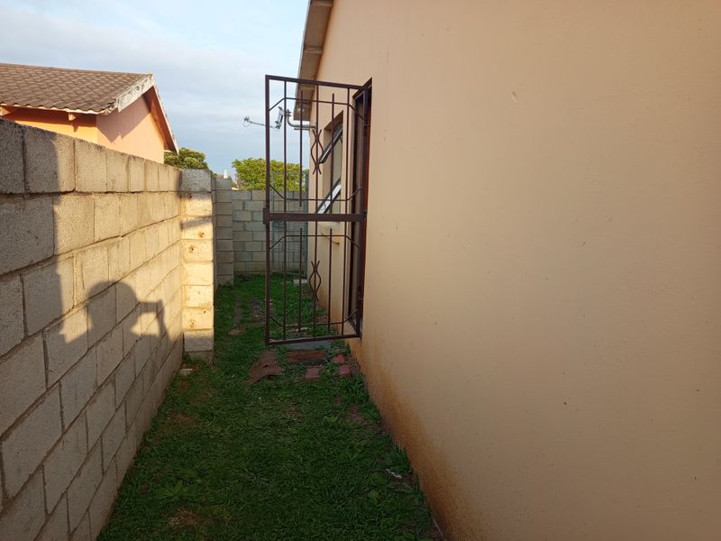 A narrow side passage of the townhouse featuring a concrete block boundary wall, security gate, and exterior wall access.