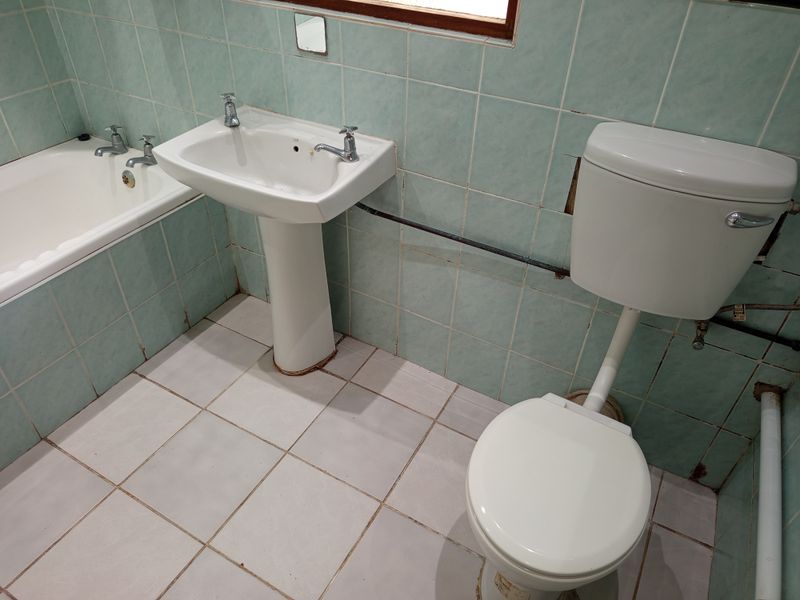 A dated bathroom featuring a pedestal basin, bathtub, and toilet with original light blue wall tiling and exposed plumbing fixtures.