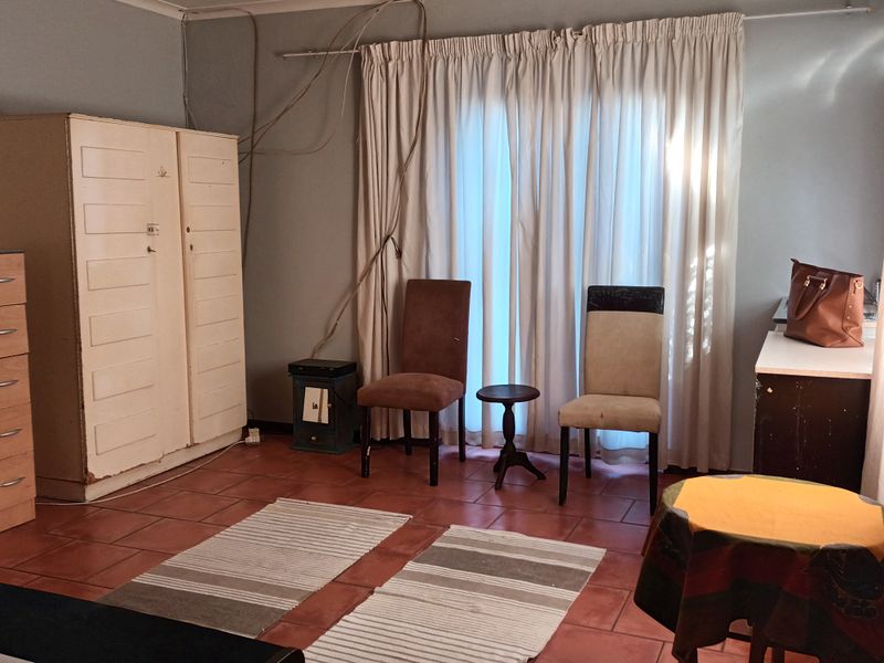 Living area featuring terracotta floor tiles and large window with curtain tracks. The space requires cosmetic updates and electrical cable management.