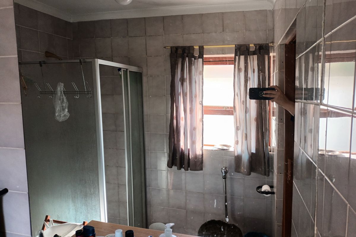 A dated bathroom featuring a shower enclosure, tiled walls, and a built-in vanity with a basin.