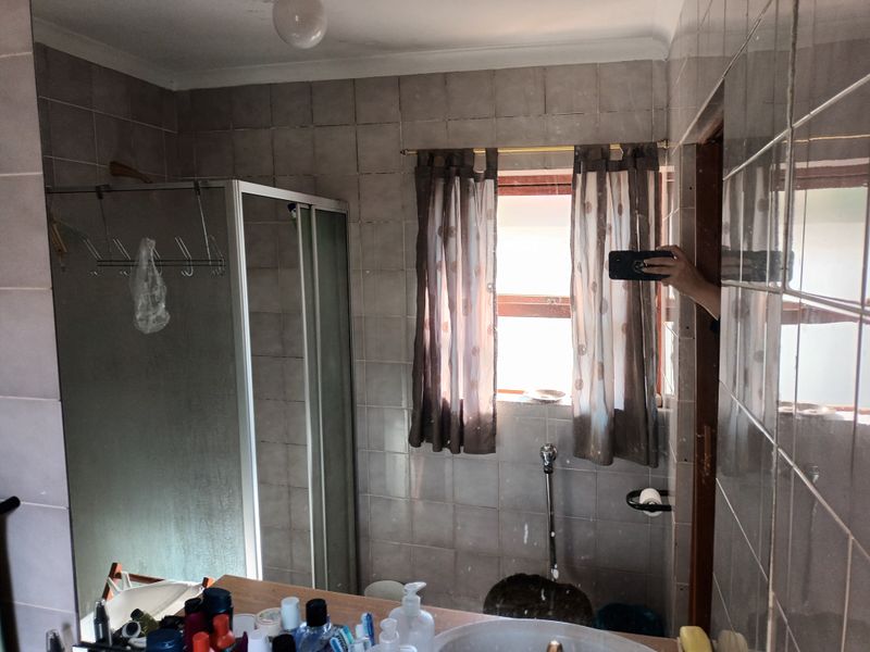 A dated bathroom featuring a shower enclosure, tiled walls, and a built-in vanity with a basin.