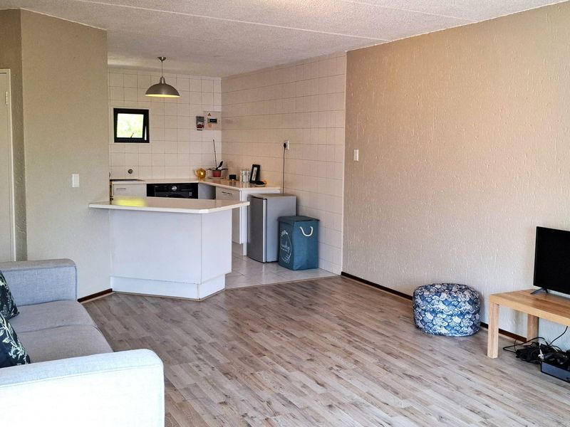 Open-plan living area featuring laminate flooring, a breakfast bar, and a functional kitchen space with tiled backsplash.