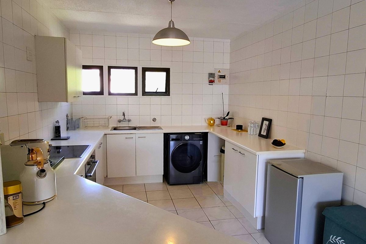 Functional kitchen featuring white cabinetry, laminate countertops, tiled walls and floors, built-in oven, and hob, providing a clean and practical workspace.