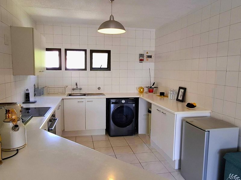 Functional kitchen featuring white cabinetry, laminate countertops, tiled walls and floors, built-in oven, and hob, providing a clean and practical workspace.