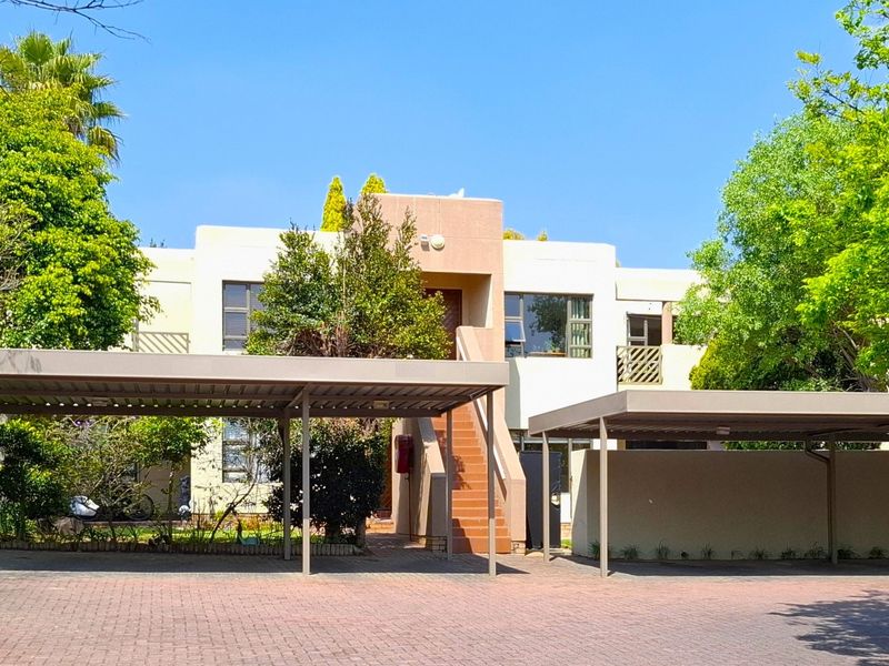 Front elevation of the apartment complex featuring covered parking bays, paved driveway, and external staircase access to upper levels.