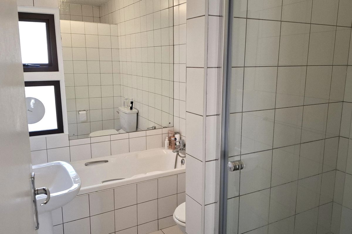 A functional bathroom featuring a pedestal basin, a built-in bathtub, a separate shower enclosure, and white wall tiling throughout.