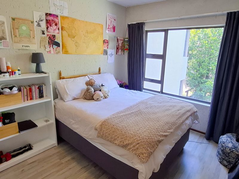A cozy bedroom featuring laminate flooring, a large window with curtains, and textured wall finishes, providing a comfortable living space.
