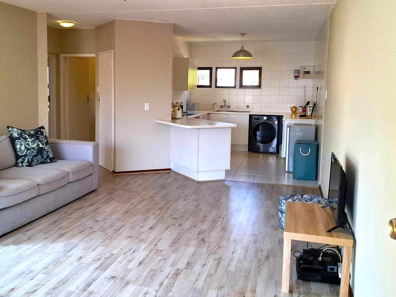 Open-plan living area featuring a functional kitchen with breakfast counter, tiled backsplash, and light-toned laminate flooring throughout the space.