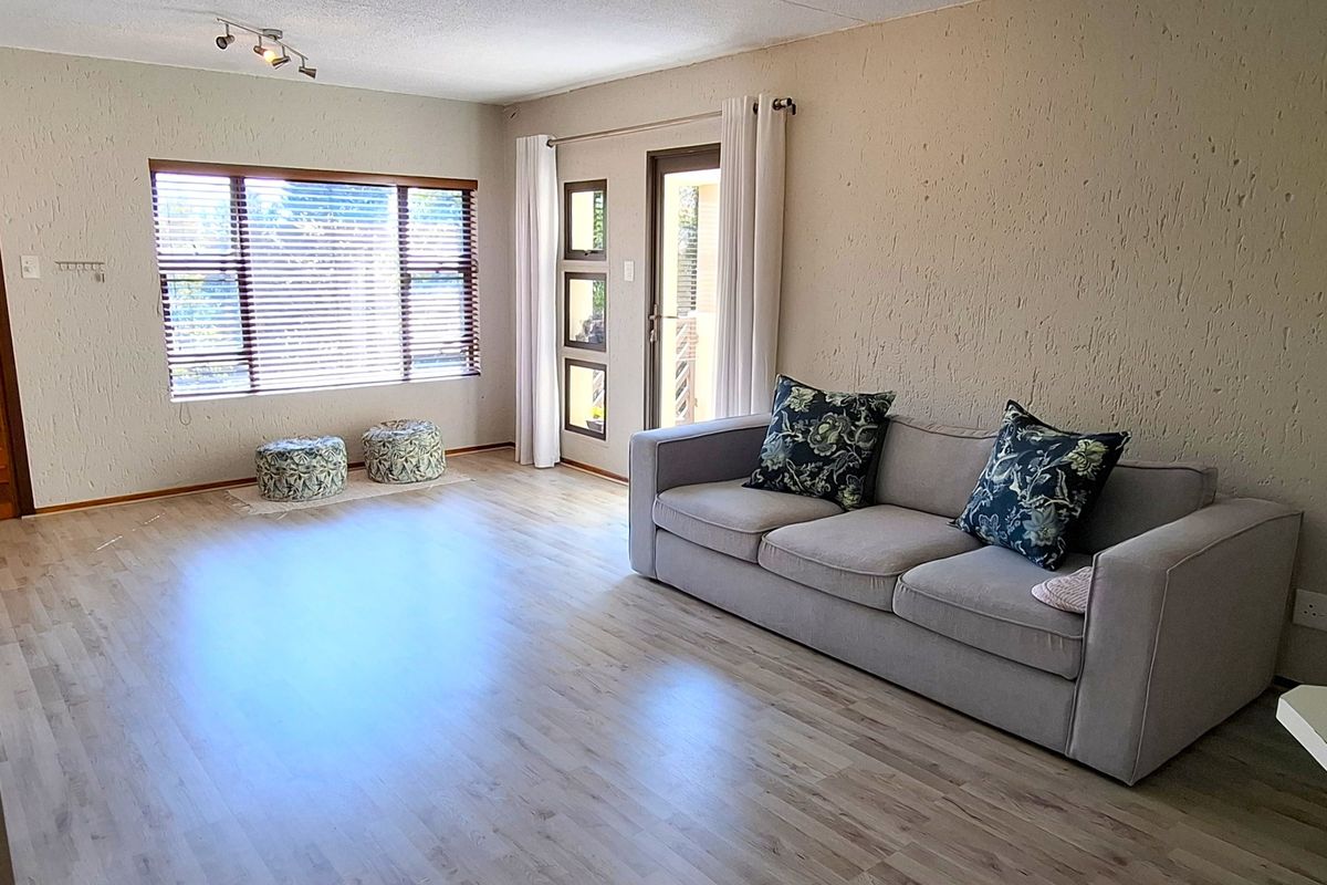A spacious living room featuring light-toned laminate flooring, textured walls, track lighting, and direct access to an outdoor area through a glazed door.