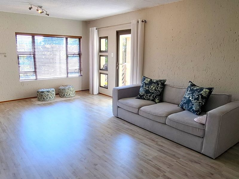 A spacious living room featuring light-toned laminate flooring, textured walls, track lighting, and direct access to an outdoor area through a glazed door.
