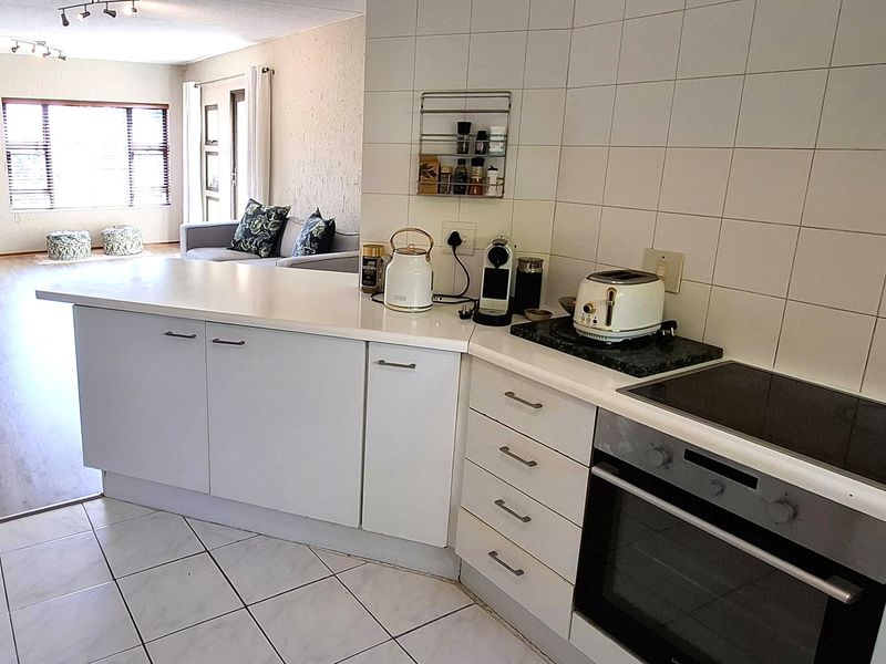 Open plan kitchen and living area featuring white cabinetry, built-in oven, electric hob, and a combination of tiled and laminate flooring.