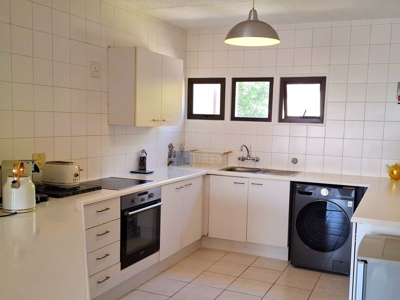 A functional kitchen featuring white cabinetry, laminate countertops, a built-in oven, electric hob, and tiled finishes throughout.