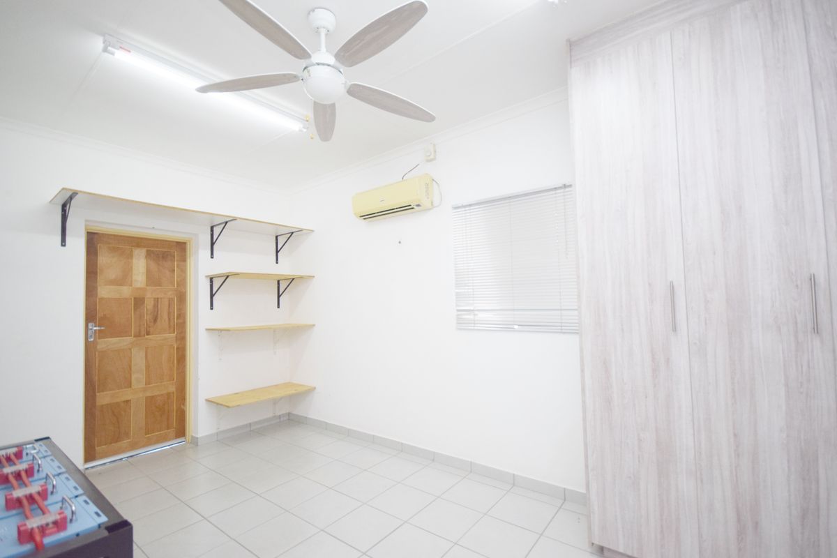 A bright, empty bedroom featuring tiled floors, a built-in wardrobe, wall-mounted shelving, a ceiling fan, and a split-system air conditioner.