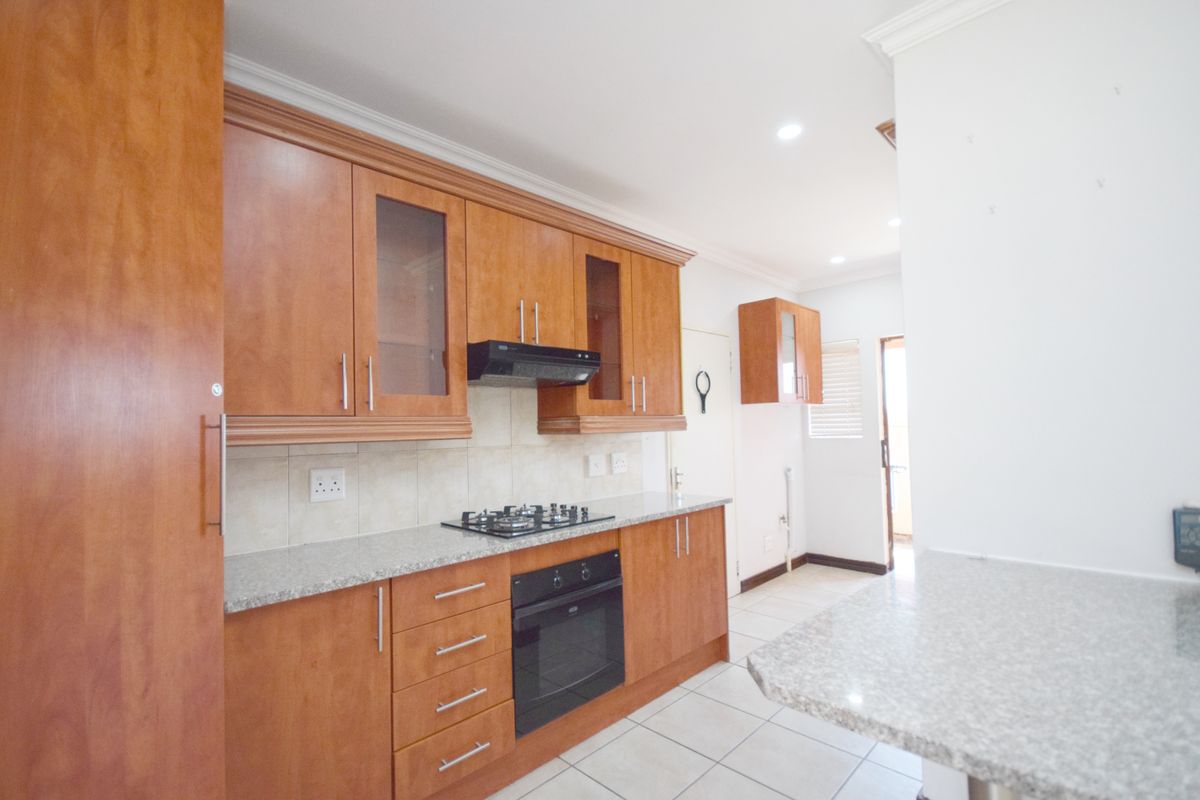 A functional kitchen featuring wooden cabinetry, granite countertops, a gas hob, built-in oven, and tiled flooring, offering a clean and practical workspace.