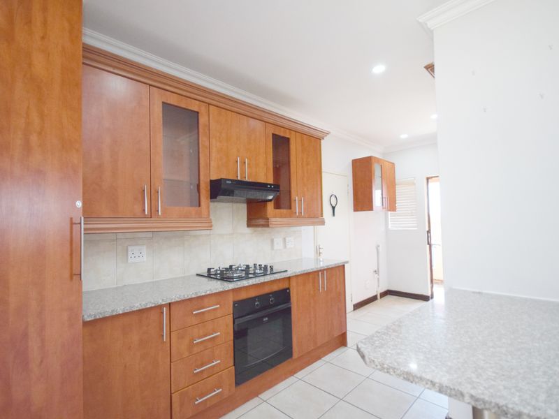 A functional kitchen featuring wooden cabinetry, granite countertops, a gas hob, built-in oven, and tiled flooring, offering a clean and practical workspace.