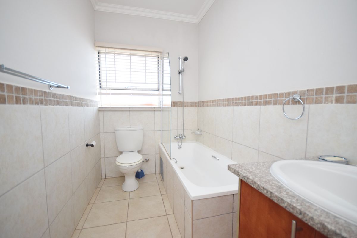 A clean, functional bathroom featuring a bathtub with a glass shower screen, a toilet, and a vanity cabinet with a granite countertop.