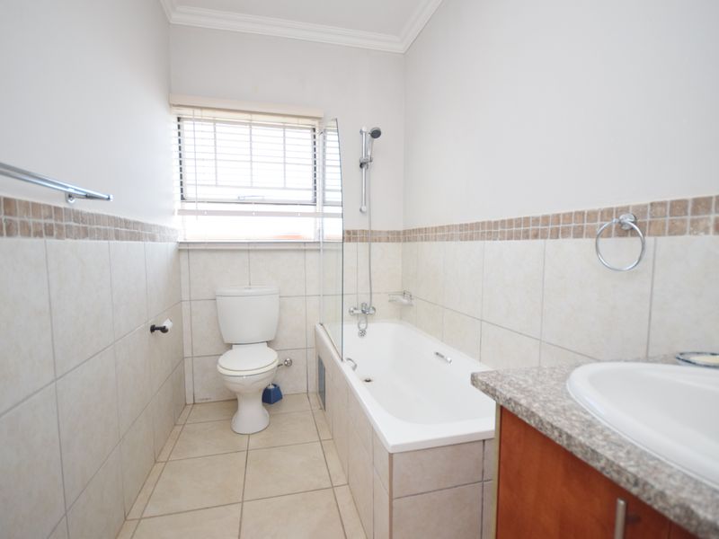 A clean, functional bathroom featuring a bathtub with a glass shower screen, a toilet, and a vanity cabinet with a granite countertop.