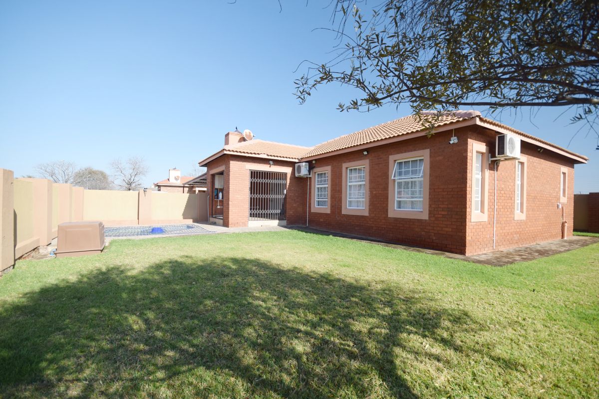Rear view of the property featuring a brick facade, tiled roof, private swimming pool, and a well-maintained lawn area.