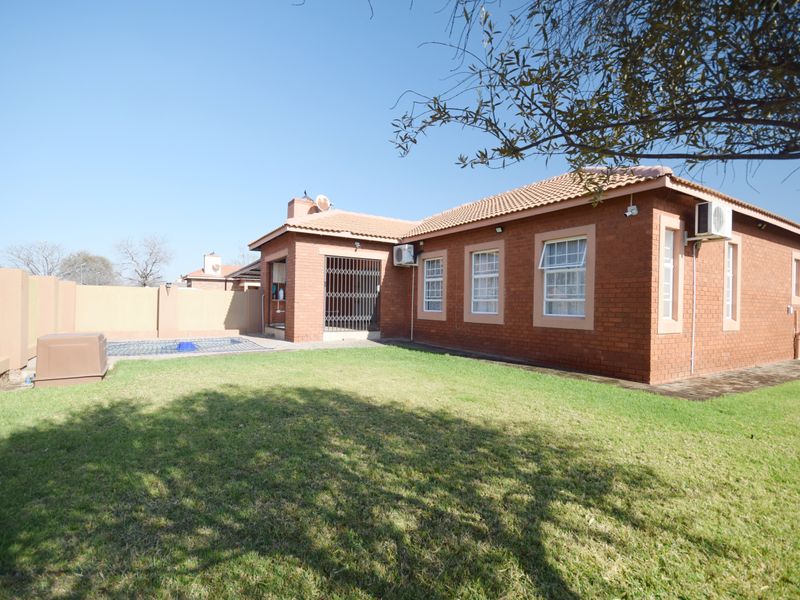 Rear view of the property featuring a brick facade, tiled roof, private swimming pool, and a well-maintained lawn area.