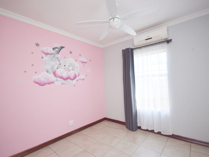A bright, empty bedroom featuring tiled flooring, a ceiling fan, and a wall-mounted air conditioning unit.