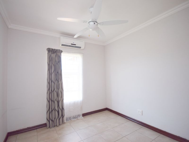 A clean, empty bedroom featuring tiled flooring, a ceiling fan, and a wall-mounted air conditioning unit.