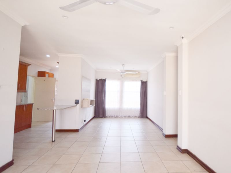 Spacious open-plan living area featuring tiled floors, a breakfast counter, and integrated kitchen cabinetry, offering a bright and versatile layout.