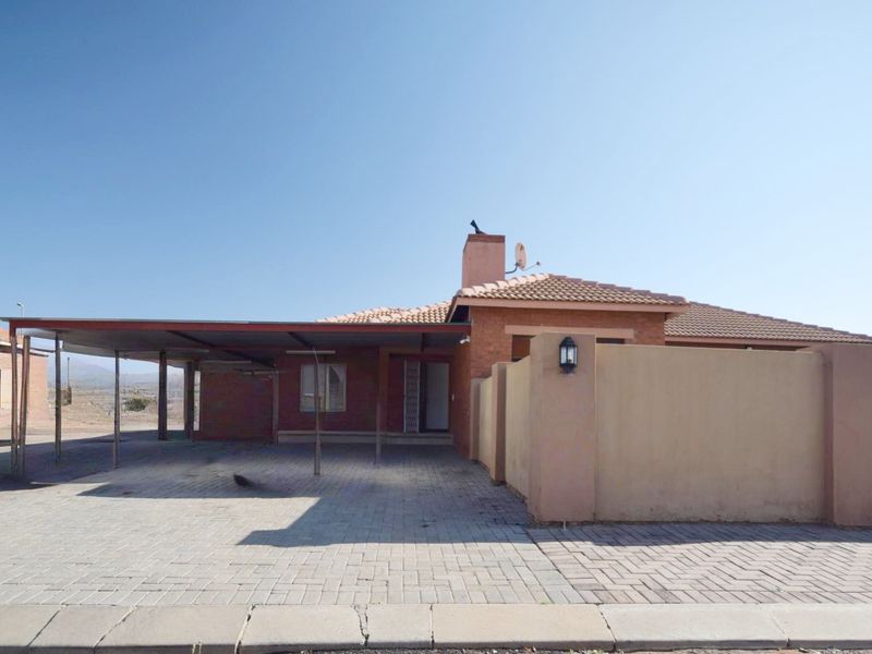 Front view of a single-story brick house featuring a paved driveway, covered carport, and a perimeter wall.