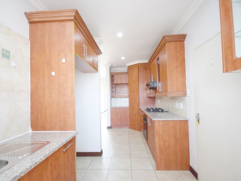 A functional kitchen featuring wooden cabinetry, granite countertops, a gas hob, and built-in oven, offering a clean and practical workspace.