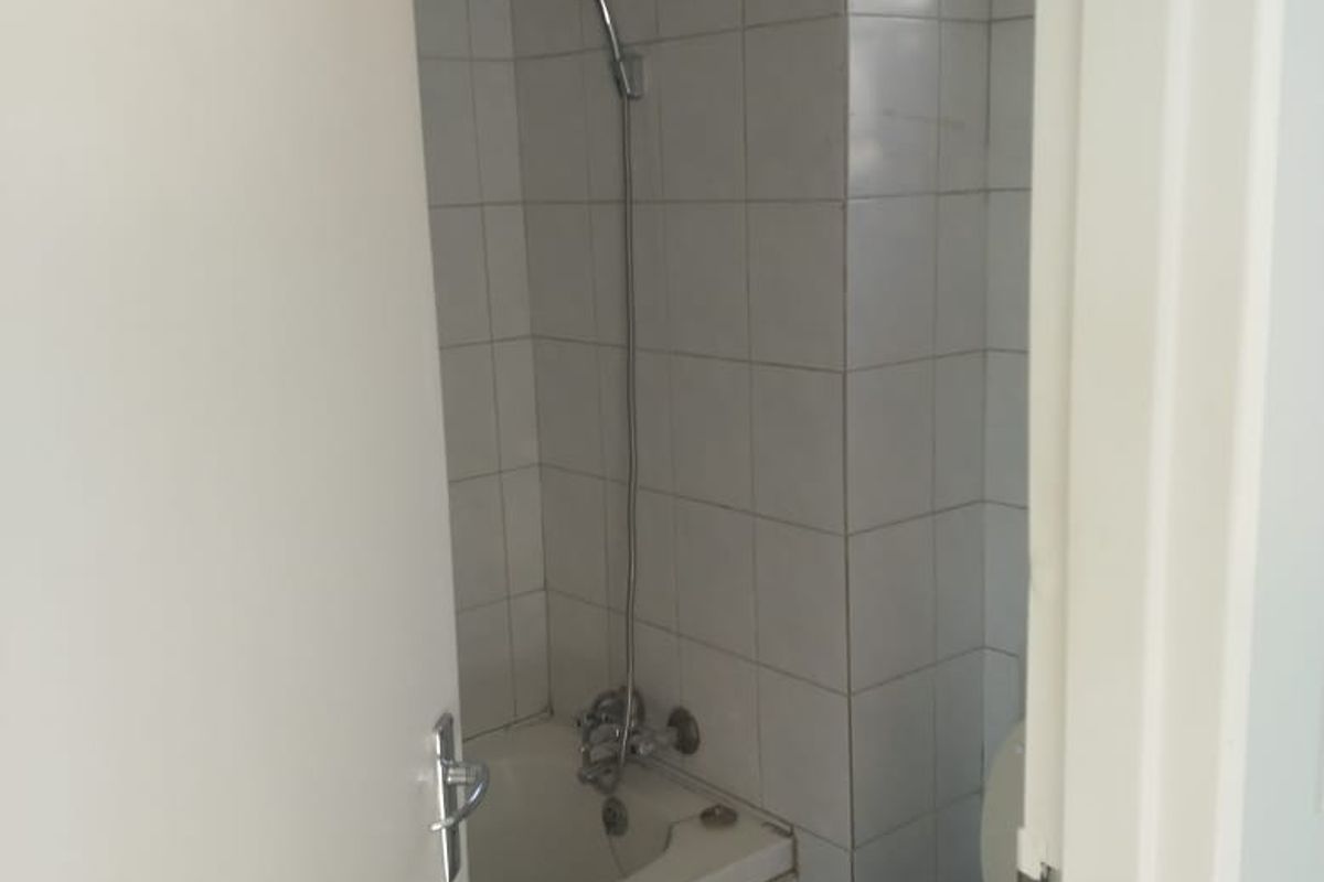 A compact bathroom featuring a built-in bathtub with shower mixer and a standard toilet, finished with white wall tiles.